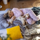 A woman cuddling with her dog in bed. A new mom recently posted moving footage of her dogs comfortin...