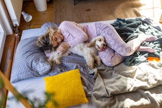 A woman cuddling with her dog in bed. A new mom recently posted moving footage of her dogs comfortin...