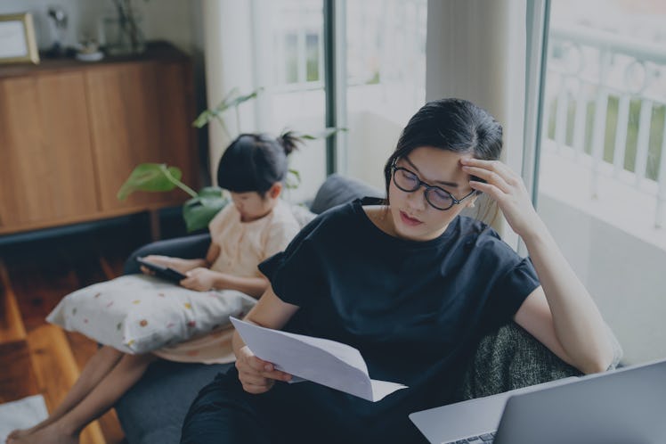 Young Asian mother looking stressed while managing her financial bills and tax documents, working fr...