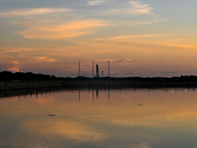 Dolphins swim as the Artemis I unmanned lunar rocket is seen behind sitting on its launch pad 39B at...
