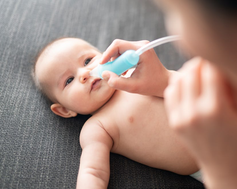 Newborn baby laying on its back with a parent holding a nasal aspirator in their nose, demonstrating...