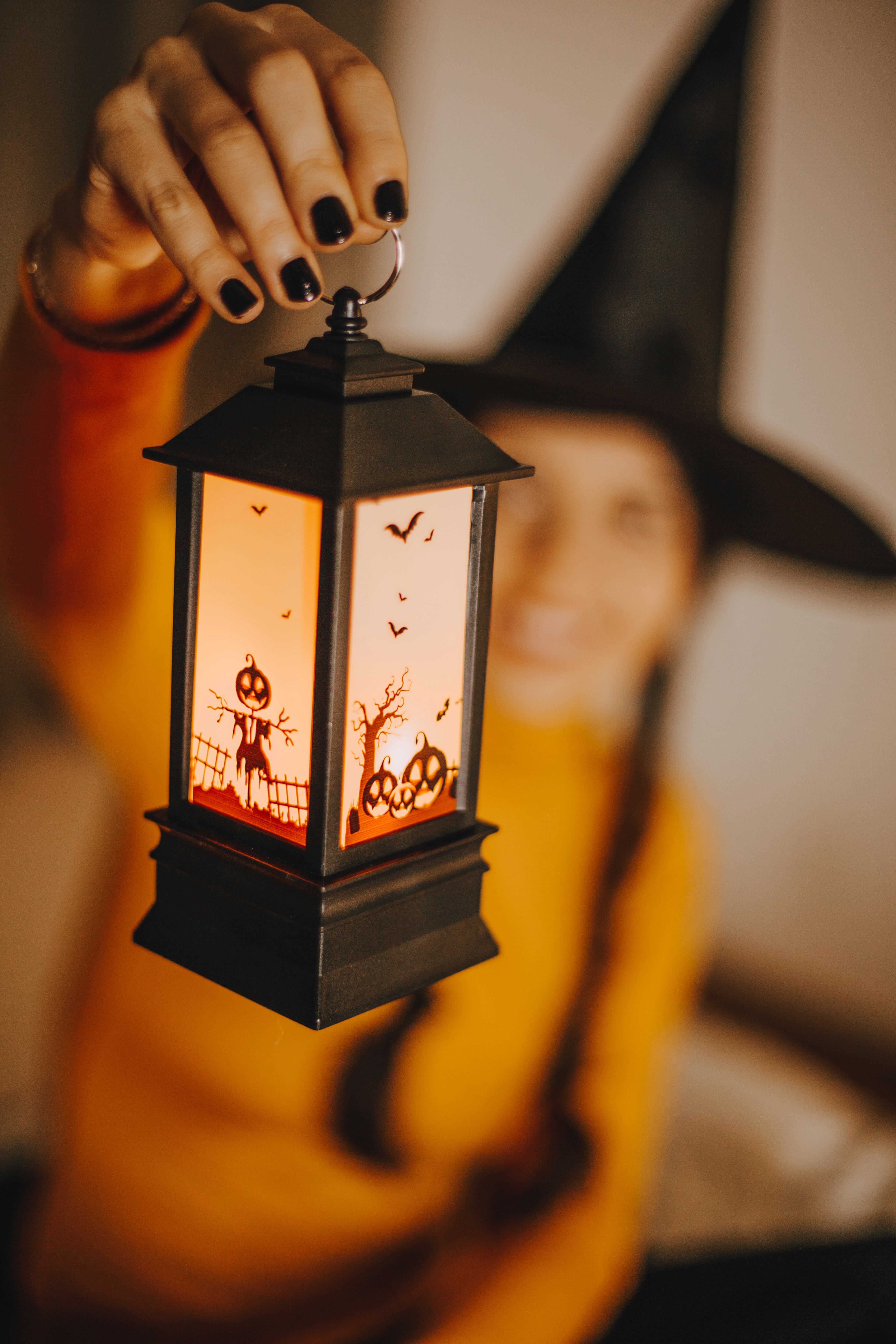 A woman in a witches hat holding up a cute Halloween lantern, one of the Halloween products to buy r...