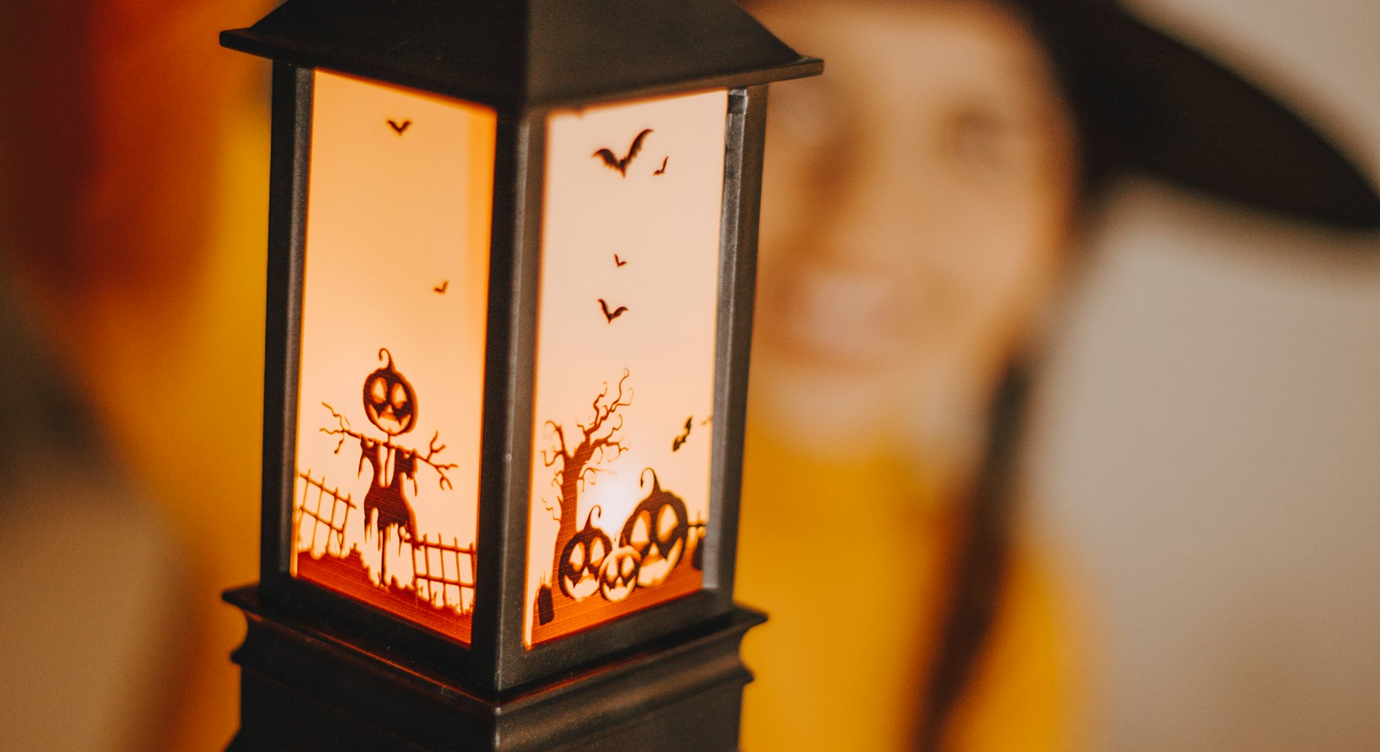 A woman in a witches hat holding up a cute Halloween lantern, one of the Halloween products to buy r...