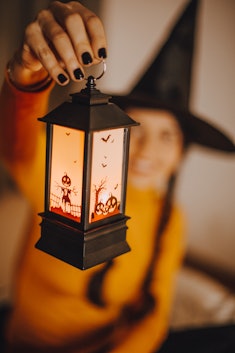 A woman in a witches hat holding up a cute Halloween lantern, one of the Halloween products to buy r...