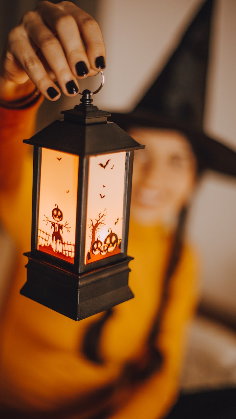 A woman in a witches hat holding up a cute Halloween lantern, one of the Halloween products to buy r...