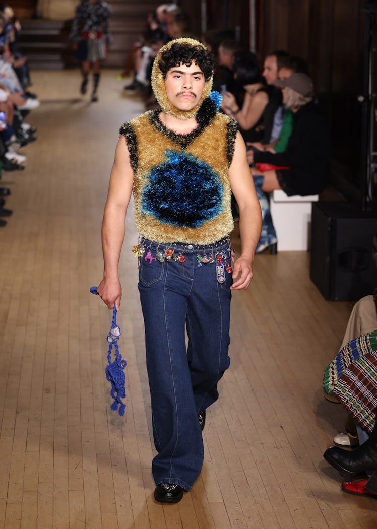 A male model walking the runway in a brown top and denim pants at the Chopova Lowena show during Lon...