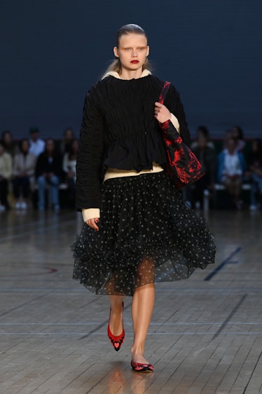 A model walking the runway in a black dress with a white belt during the Molly Goddard show 