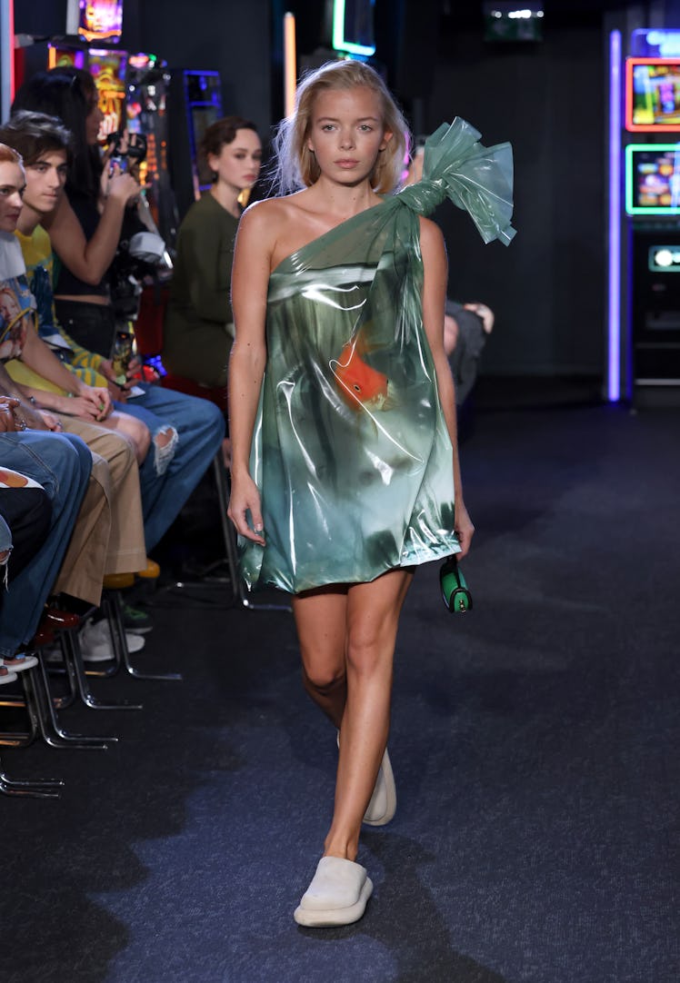 A model walking the runway in a green nylon mini dress at the JW Anderson show