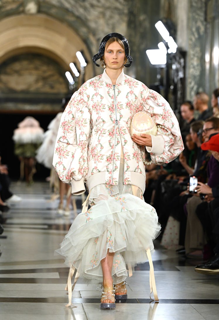 A model walking the runway while wearing a white jacket and dress during the Simone Rocha show durin...