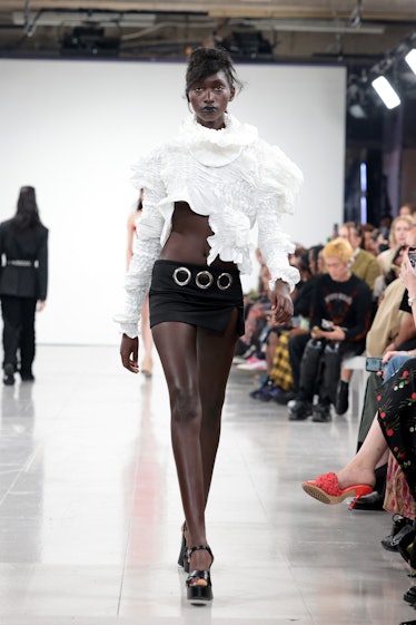A model walking the runway while wearing a white fur top and black shorts at the Feben show during L...