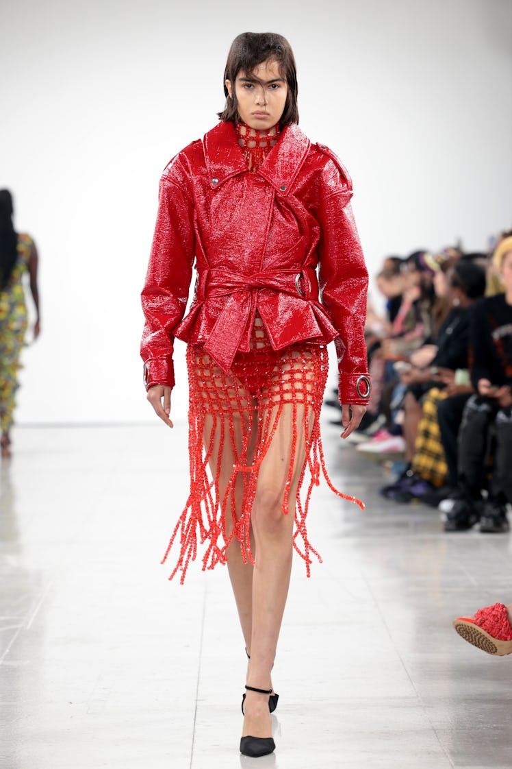 A model walking the runway in a red leather jacket and dress at the Feben show during the London Fas...