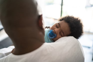 Father putting baby son to sleep on his arms at home.