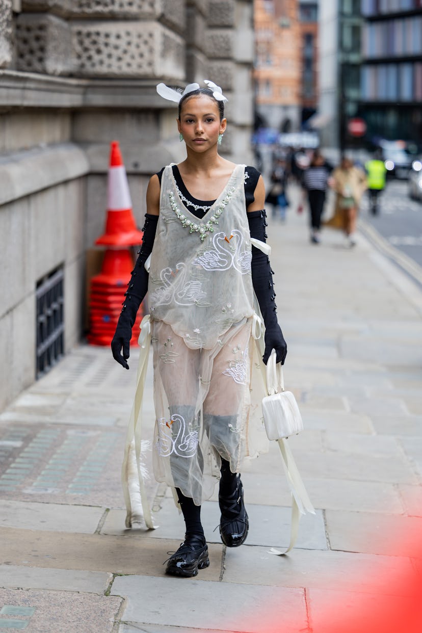 A guest wears black gloves, see through dress, white bag outside Simone Rocha during London Fashion ...