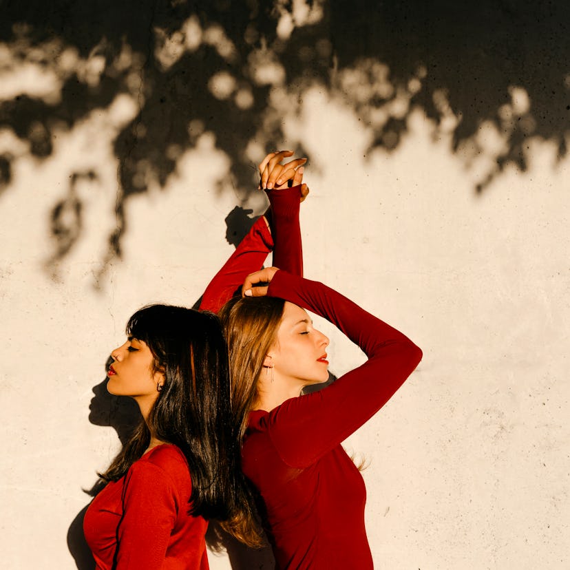 two young women back to back linking hands as they discuss the new moon in libra on sept. 25, 2022