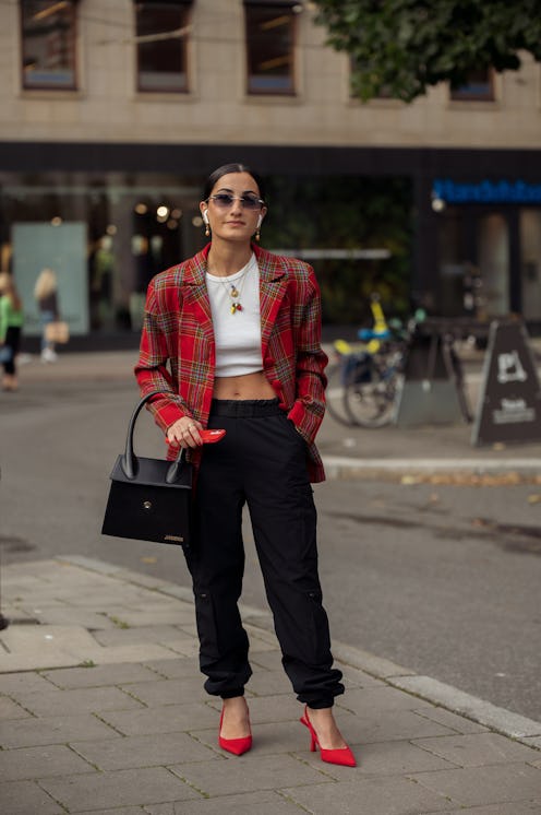 STOCKHOLM, SWEDEN - AUGUST 31: A guest wearing black cargo pants, white crop top, red jacket, red s...