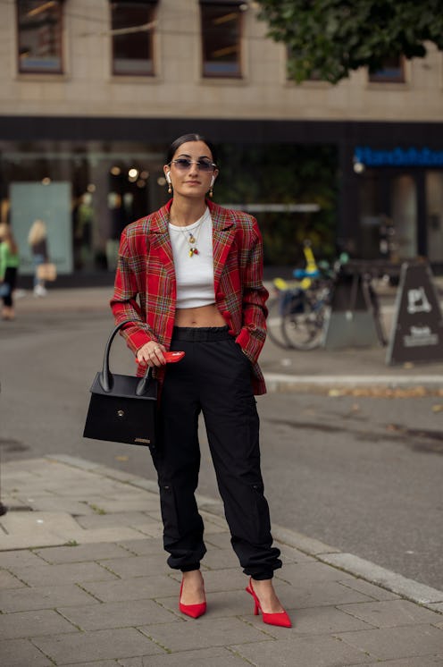 STOCKHOLM, SWEDEN - AUGUST 31:  A guest wearing black cargo pants, white crop top, red jacket, red s...