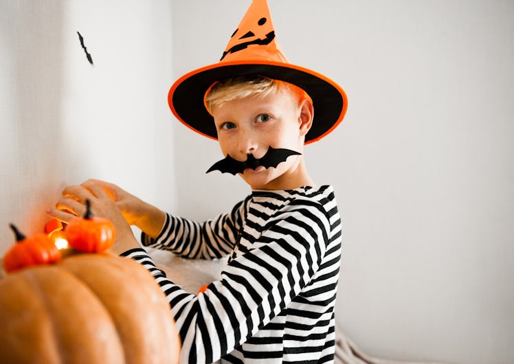 Halloween kids. Portrait Laughing boy with pumpkin face mask in witch costume hat with candy bucket ...