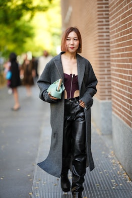 MILAN, ITALY - SEPTEMBER 21: A guest wears a gray oversized long coat, a burgundy zipper / shoulder-...