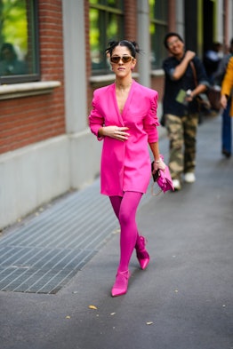MILAN, ITALY - SEPTEMBER 21: A guest wears sunglasses, earrings, a neon pink long blazer jacket dres...