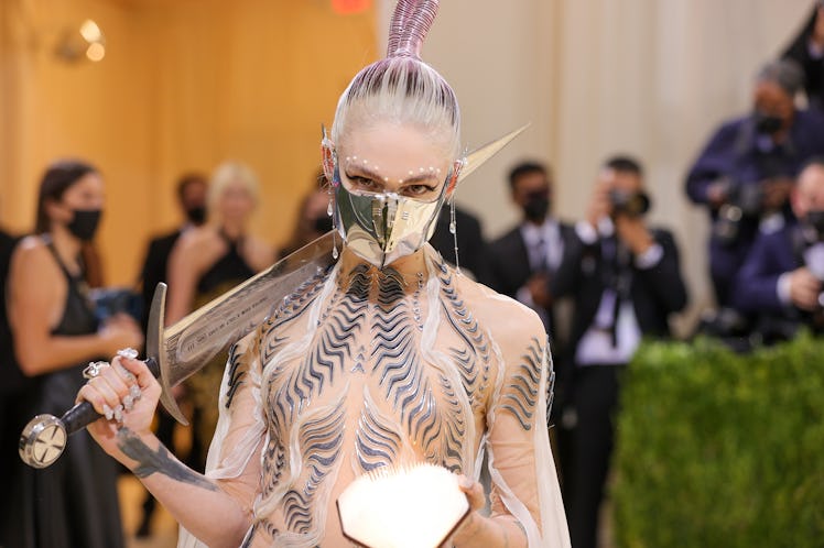 Grimes at the 2021 Met Gala; carrying a sword, a glowing orb and a metallic mask