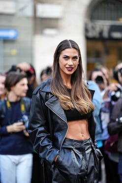 MILAN, ITALY - SEPTEMBER 21: A guest wears a black shiny leather long trench coat, black shiny leath...