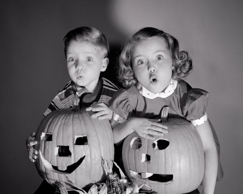 1950s Boy And Girl Standing Above Four Jack-O-Lanterns Halloween Carved Pumpkins With Scared Frighte...
