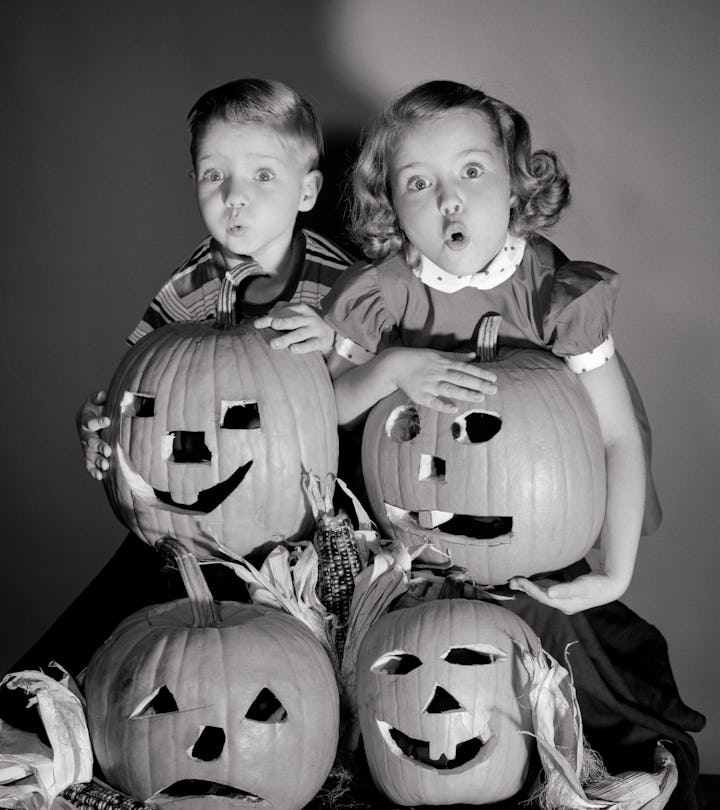 1950s Boy And Girl Standing Above Four Jack-O-Lanterns Halloween Carved Pumpkins With Scared Frighte...