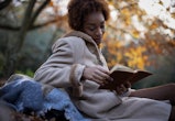Young woman in brown coat reading book in autumn park