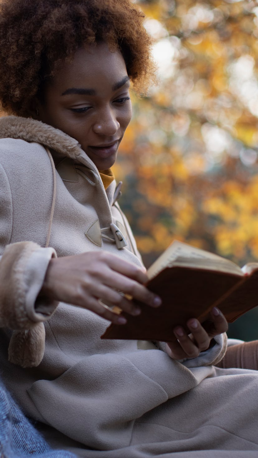 Young woman in brown coat reading book in autumn park