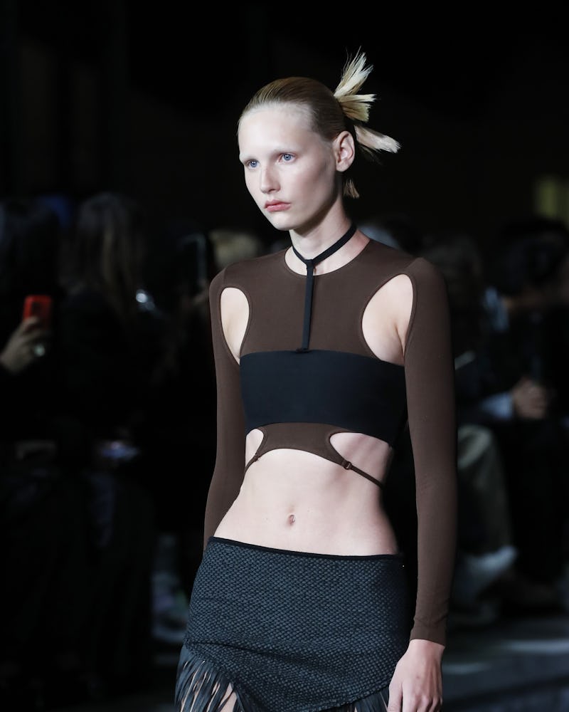 The model wears a strappy top with cutouts paired with a fringed black skirt by Andreadamo.