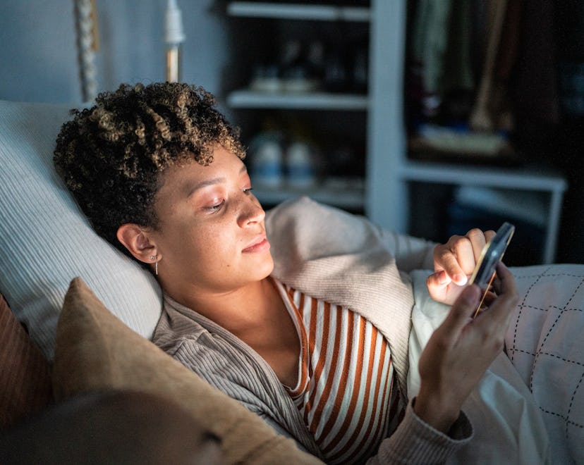 Young woman using smartphone on the bed in an article of up in the middle of the night instagram cap...