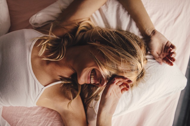 Portrait of a young beautiful woman waking up, with a smile on her face hair on pillow in an article...