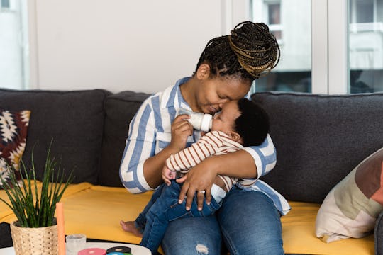 Portrait of a happy African American woman holding and feeding her cute baby boy and enjoying mother...