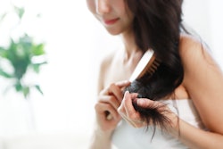 a woman brushing her long, dark hair in an article about how much hair loss is normal and how to kno...