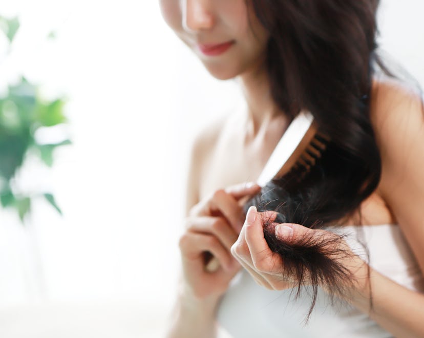 a woman brushing her long, dark hair in an article about how much hair loss is normal and how to kno...