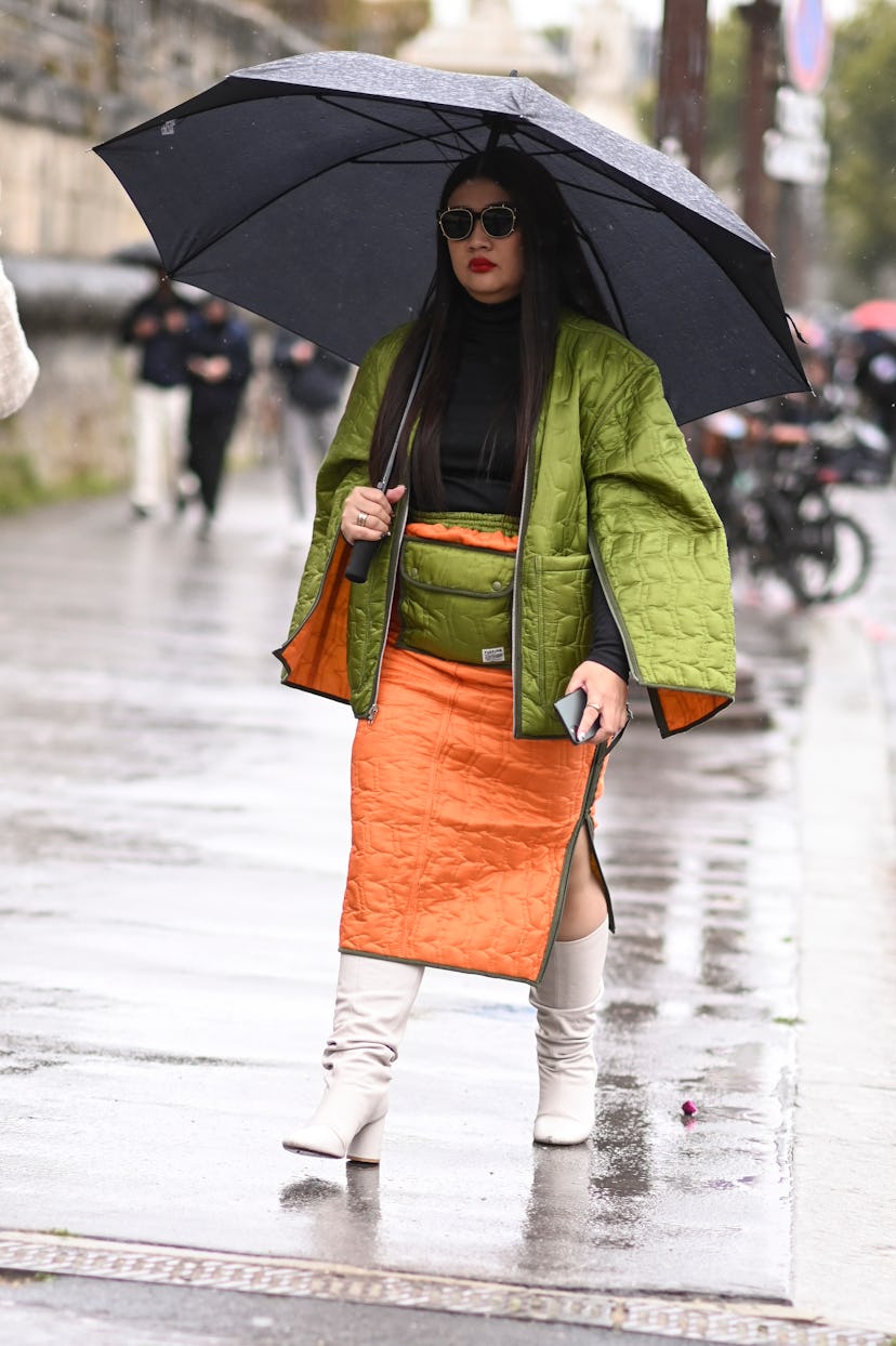  A guest is seen wearing a green coat, black top, green and orange skirt and white boots.
