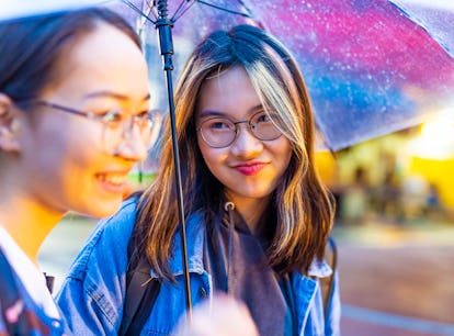 young people who learned how to style your hair in humidity standing outside under an umbrella.