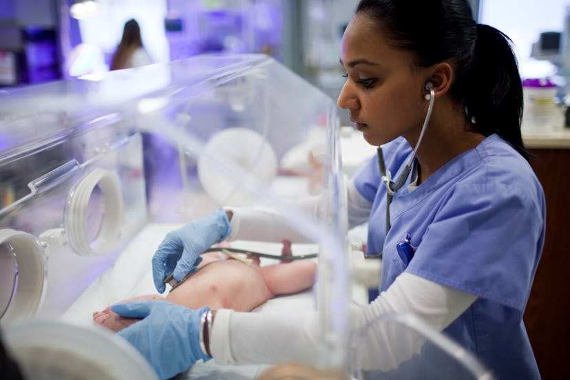 A hospital care provider checking on a NICU baby alone in an incubator. 