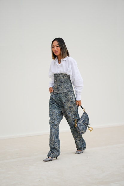 Aimee Song wears a white pearls necklace, a white oversized shirt, a blue and beige denim embroidere...