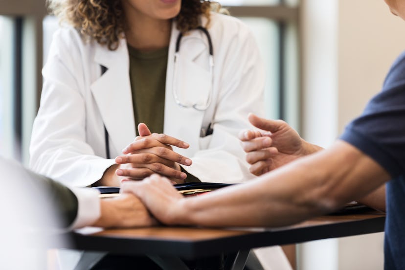 Unrecognizable female doctor sits with clasped hands across from unrecognizable couple.  in an artic...