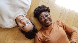 Two women laying on their backs as they smile at the camera and discuss their October 10, 2022 weekl...