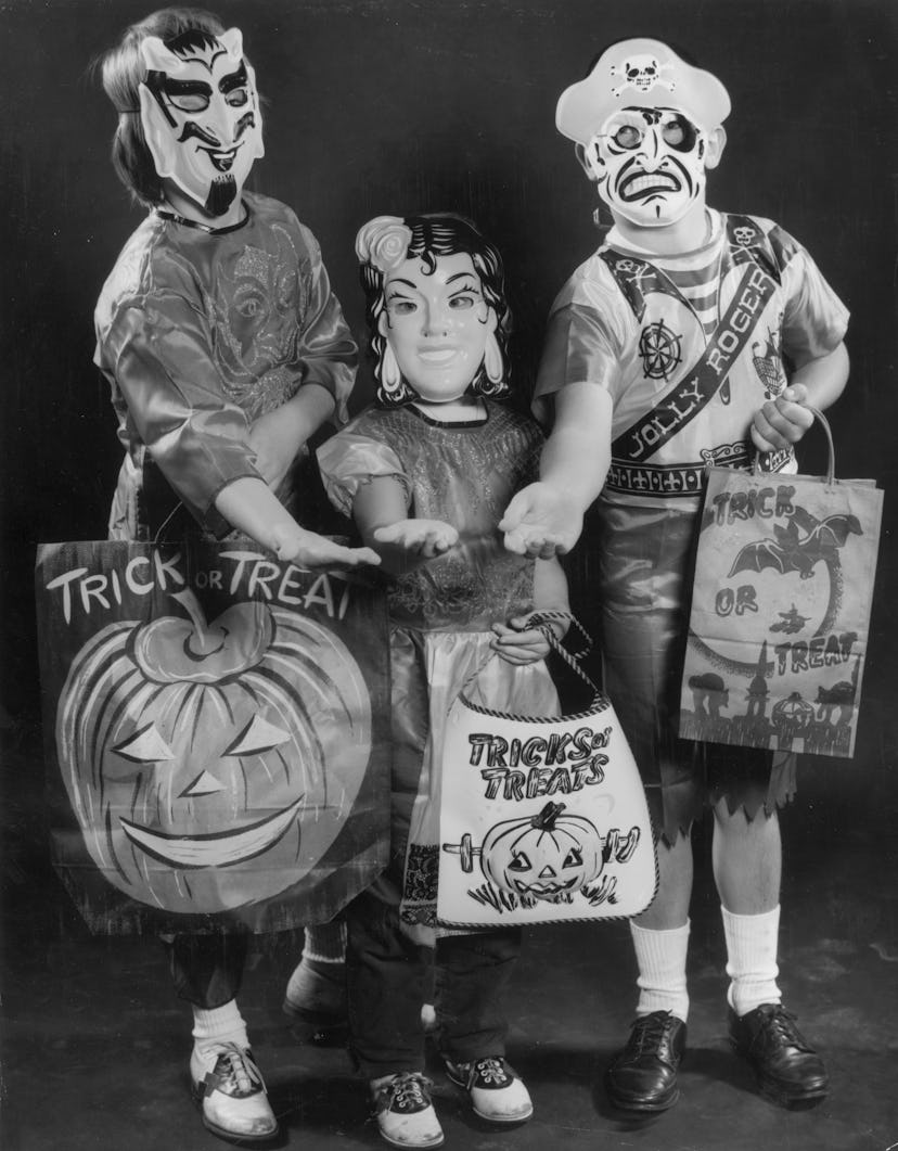 Full-length portrait of three children wearing Halloween costumes and holding trick-or-treat bags in...