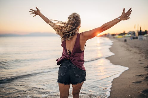 Woman running on the beach in the shallow water with her hands up in the sky. She is running towards...