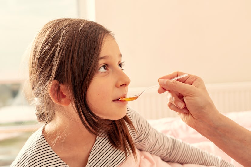 Mother giving honey to little girl to stop kid's cough