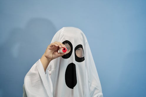 Close-up of a little boy dressed as a ghost in his room showing a candy eye to frighten and scare hi...