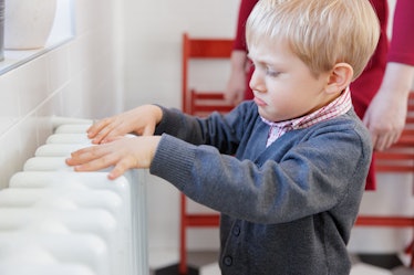 A child touching a radiator, frowning.