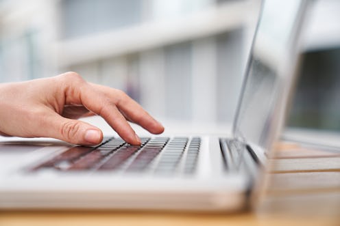 Close-up side view shot of woman's hand typing on an out of focus laptop computer