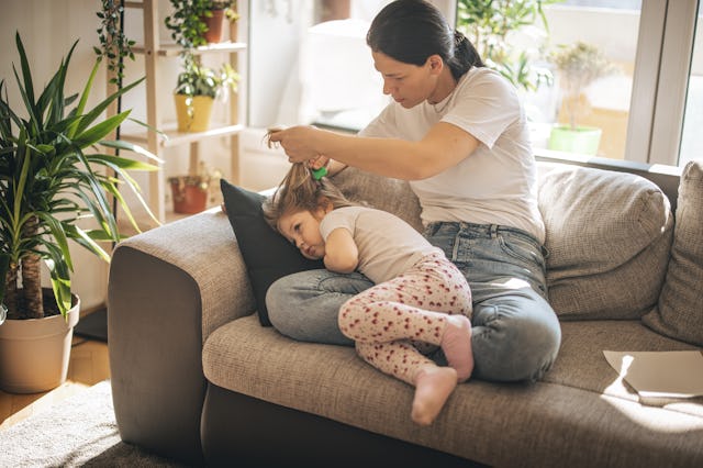 A mom checks her daughter for head lice. New guidance from the AAP states that kids with lice should...