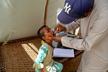 A health worker administers polio vaccine drops to a child inside a tent of internally displaced flo...