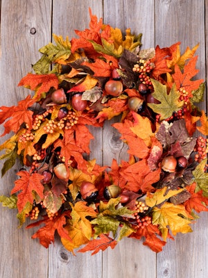 A beautiful fall wreath with orange and yellow leaves on a wooden plank background.